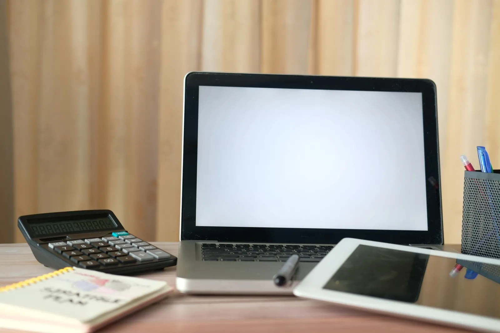 A laptop, calculator, tablet and notebook on a desk