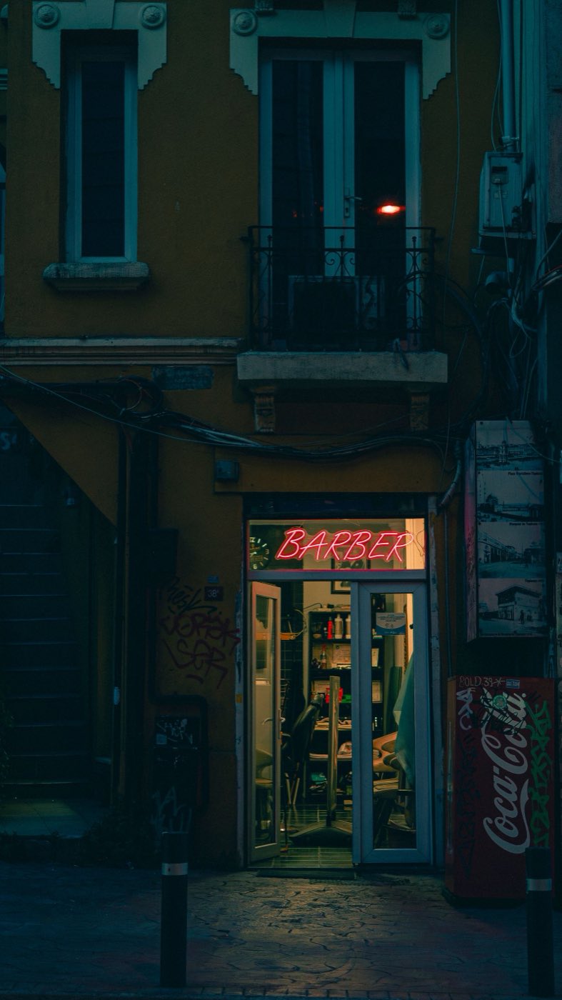A lit barbershop doorway with a neon BARBER sign on a dark street