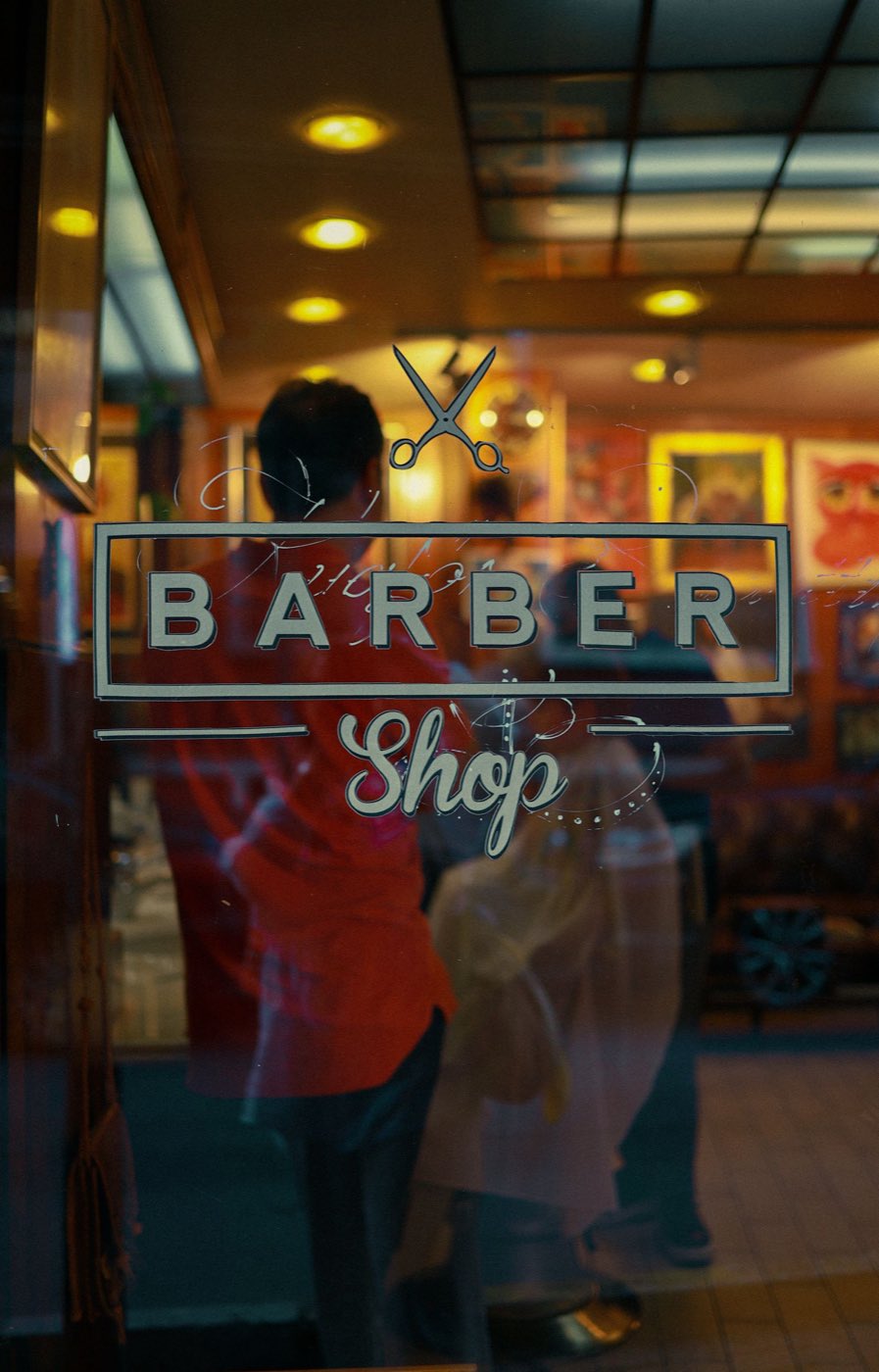 A barbershop window decal seen from the street, warm light inside