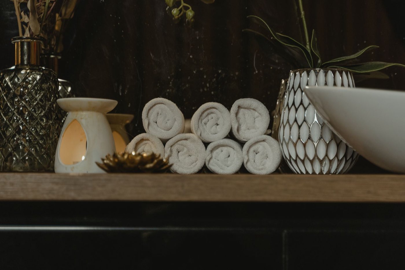 Rolled towels and a warm candle on a spa shelf