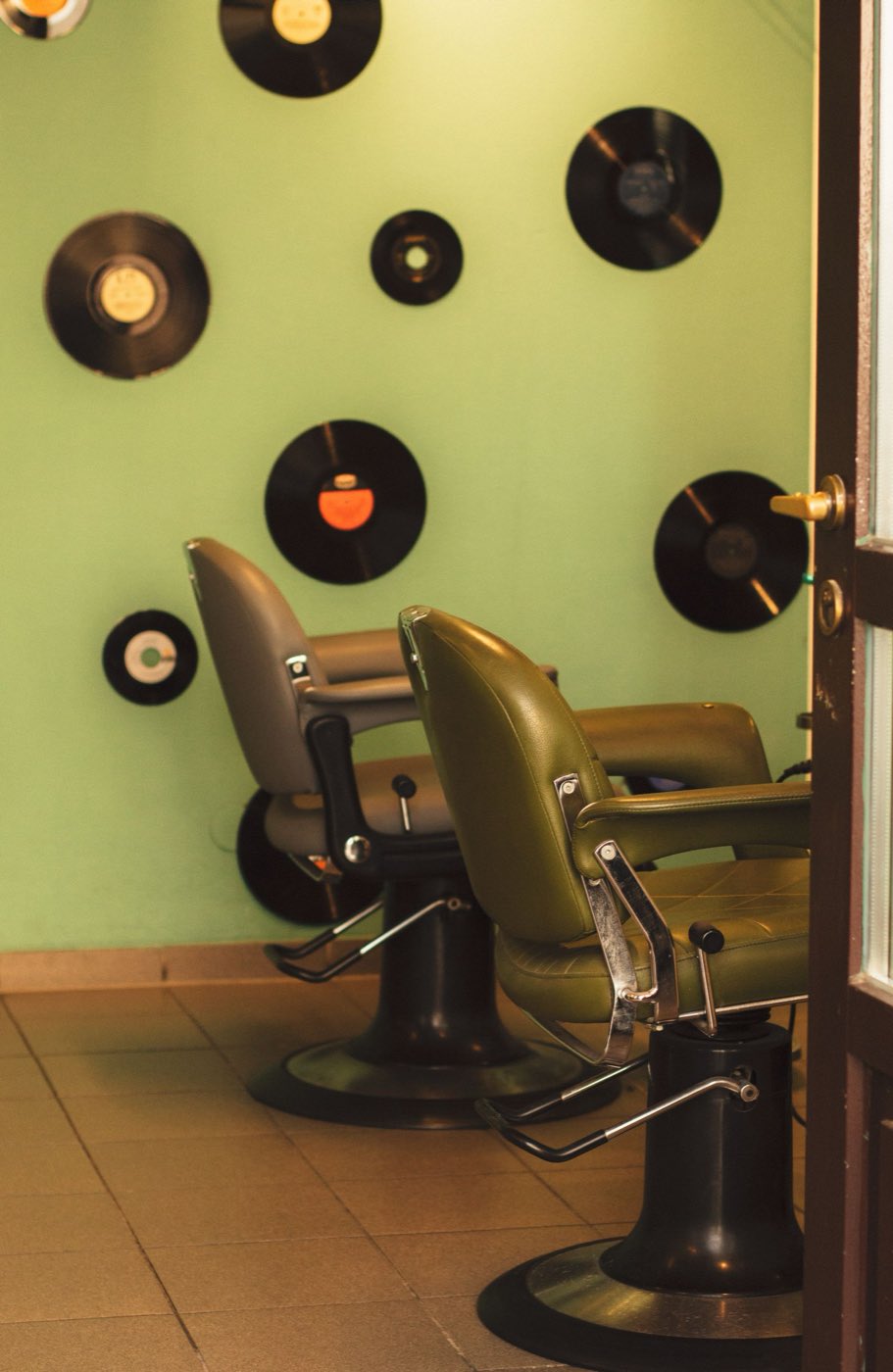 Vintage barber chairs against a green wall decorated with vinyl records